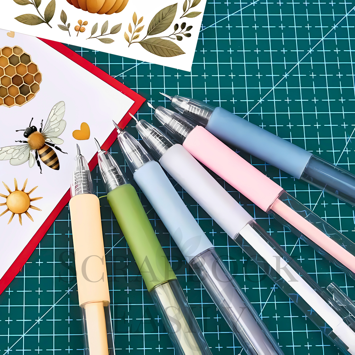 Array of precision craft knife pens in pastel colours displayed on a cutting mat, with scrapbooking cardstock featuring bee & botanical designs, ideal for intricate paper cutting & detailed scrapbooking projects, available for online purchase.